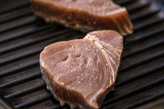 Close up of chargrilled tuna steaks cooking in a griddle pan with seasoning