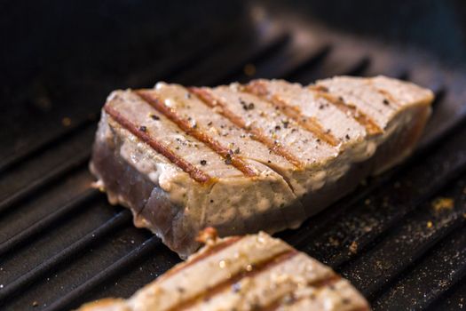 Close up of chargrilled tuna steaks cooking in a griddle pan with seasoning
