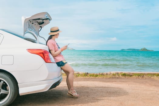 Women hold a smartphone sitting with a beach car