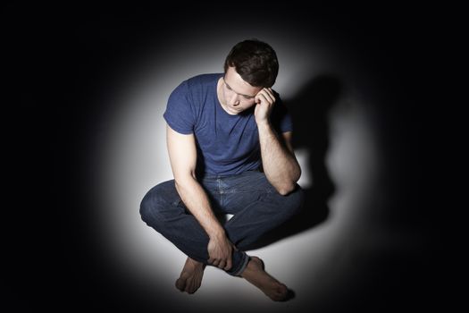 Unhappy Young Man Sitting In Pool Of Light