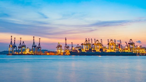 Freighter ship loading cargo at loading dock on twilight time. Singapore, south east asia.