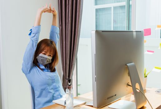 Work from home concept, Happy Asian beautiful young business woman wearing face mask protective quarantines disease coronavirus or COVID-19 her stretching her arms above her head after success work