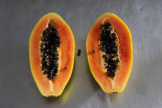 Papaya fruit cut in half on the kitchen table. Gray metal kitchen table background.