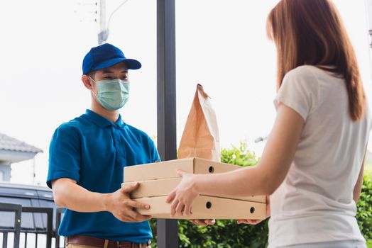 Asian delivery express courier young man giving paper bags fast food and pizza box to woman customer receiving both protective face mask, under curfew quarantine pandemic coronavirus COVID-19