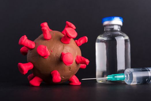 Closeup plasticine disease cells virus bottle vaccine and syringe of coronavirus outbreak and coronaviruses influenza flu, studio shot isolated on black background, pandemic COVID-19 medical health