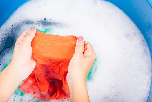 Closeup young Asian woman use hands washing color clothes in basin with detergent have soapy bubble water, studio shot background, laundry concept