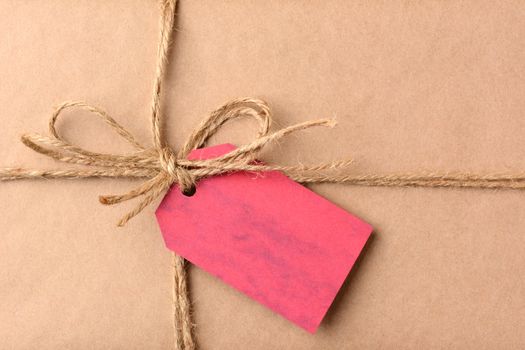 Closeup of a gift tag on a Christmas present. The package is wrapped in plain brown paper and twine. The red tag is blank. Horizontal format.