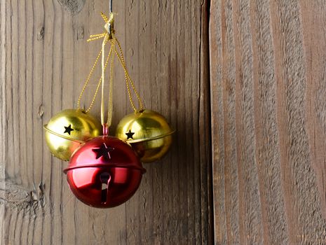 Red and Gold Jingle Bells hanging on a rustic wooden wall. 