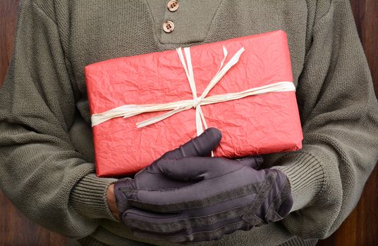 Closeup of a man wearing a sweater and gloves holding a wrapped Christmas present in front of his torso. Man is unrecognizable. Horizontal format.