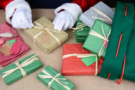 Closeup of Santa Claus wrapping presents. Only Santa's hands are visible as he puts the finishing touches on a variety of gift boxes next to his bag on Christmas Eve. Horizontal Format.