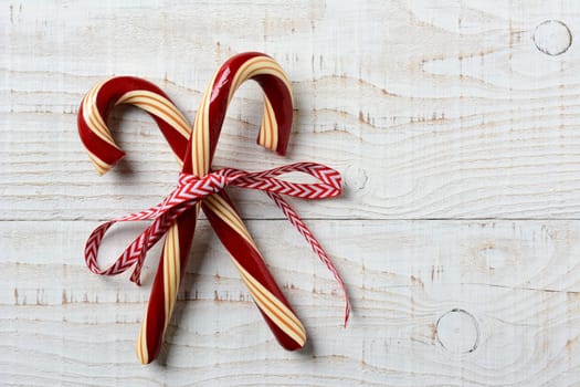 Closeup of two old fashioned candy canes on a rustic whitewashed wooden table. The treats are crossed and tied with a red and white ribbon, Horizontal format with copy space.