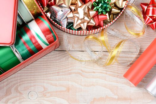 High angle closeup shot of two tins of ribbons and bows on a white wood table. Horizontal format with two rolls of wrapping paper and copyspace.