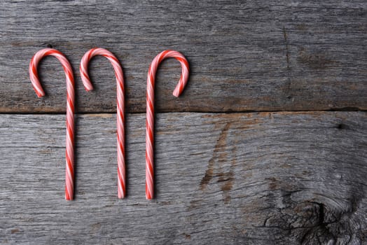 High angle shot of three holiday candy canes on a rustic wood table. Horizontal format with copy space.