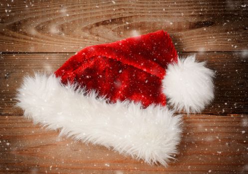Santa Claus Hat on a rustic wooden floor with snow flakes and an instagram retro look. High angle view with vignette.