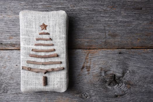 Overhead shot of a burlap wrapped Christmas present with a twig tree and star on a rustic wood table, with copy space.