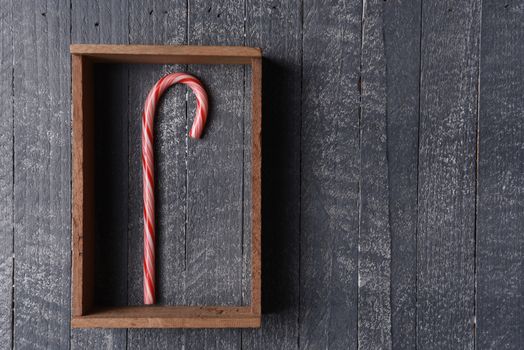 A candy cane in a wood frame on gray rustic wall.