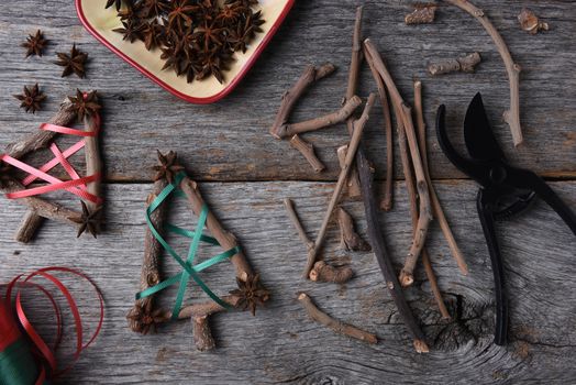 Top view of the equipment and supplies for making rustic Christmas decorations, including twigs, star anise, shears, and ribbon.