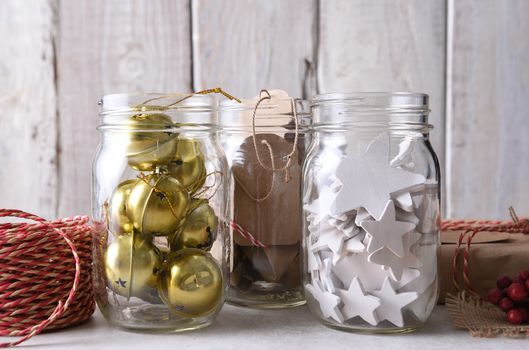 Christmas present wrapping supplies. Closeup of three mason jars with gift tags, wood stars, and sleigh bells against a rustic white wood wall.