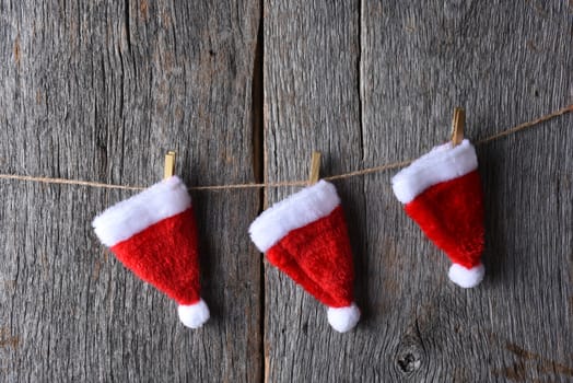Three Santa hats hanging from a piece of twine stretched across a rustic wood wall.