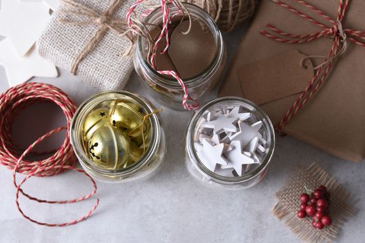 Christmas present wrapping supplies. High angle shot of three mason jars with gift tags, wood stars, and sleigh bells agains a rustic white wood wall.