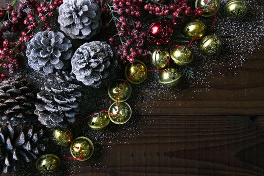 Jingle bells, pine cones and red berries on a rustic wood table with snow. Horizontal format with copy space. 