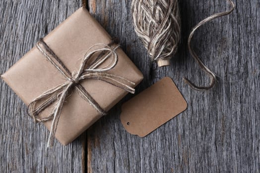 Top view of a plain wrapped Christmas present on a rustic wood table with twine and a blank tag.