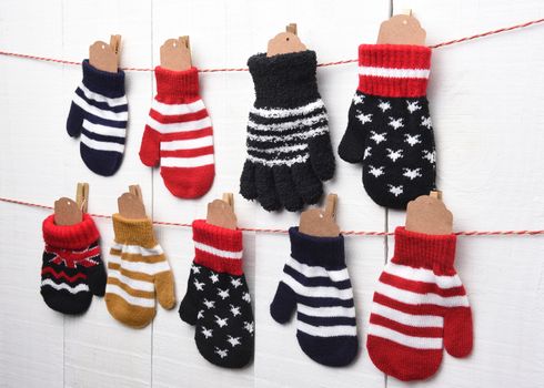 Christmas Advent Calendar: Mitten and Gloves hanging on string and clothes pins against a white wall. Blank tags are in the mittens ready for your copy. 