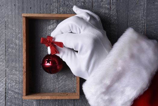 Santa Claus hanging a red jingle bell inside a wood frame on gray wood wall.