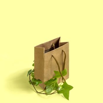 Eco-friendly shopping bag with branch of green plant on yellow background. Use paper bags instead of plastic, zero waste. Concept of social responsibility and environmental protection
