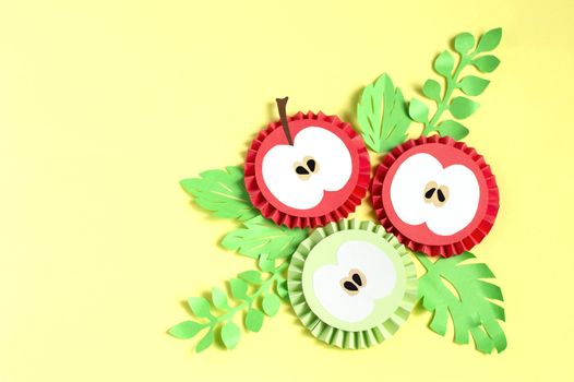 Colorful paper apple slices and leaves on yellow background. Paper art and craft