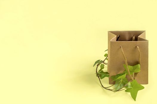 Eco-friendly shopping bag with branch of green plant on yellow background. Use paper bags instead of plastic, zero waste. Concept of social responsibility and environmental protection