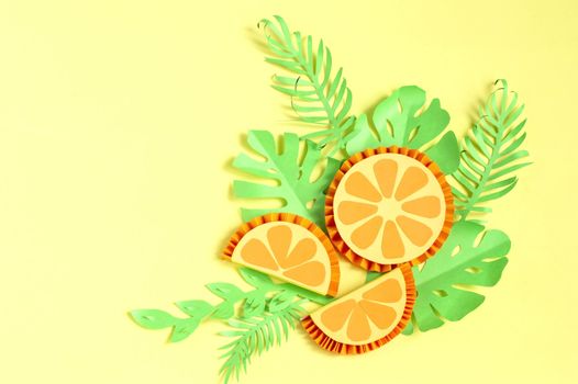 Colorful paper slices of orange with paper tropical leaves on yellow background. Paper art and craft