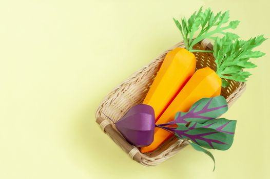 Colorful paper carrot and beet in wicker tray on yellow background. Real volumetric handmade paper objects. Paper art and craft