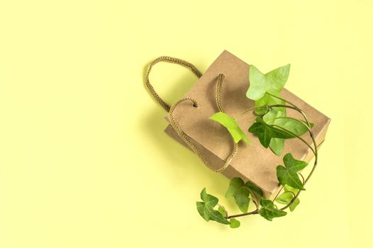 Eco-friendly shopping bag with branch of green plant on yellow background. Use paper bags instead of plastic, zero waste. Concept of social responsibility and environmental protection