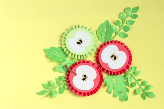Colorful paper apple slices and leaves on yellow background. Paper art and craft