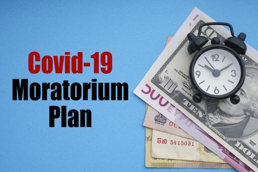 COVID19 MORATORIUM PLAN text with alarm clock and banknotes currencies on blue background. Coronavirus Covid19 and Business Concept