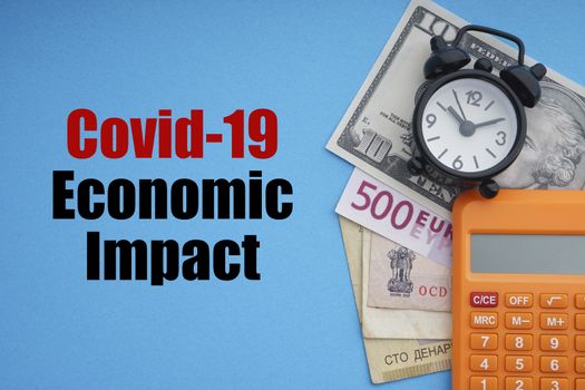 COVID19 ECONOMIC IMPACT text with alarm clock, banknotes currencies  and calculator on blue background. Coronavirus Covid19 and Business Concept
