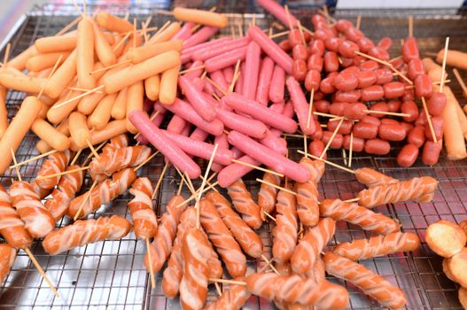 A variety of hot dog fries and skewers are stacked on top of the grill for sale.