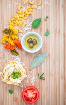 Italian food concept pasta with vegetables olive oil and spices herbs parsley , basil ,bay leaves and rosemary set up with white cheese on wooden background.