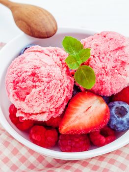 Close Up ice cream mixed berry fruits raspberry ,blueberry ,strawberry and peppermint leaves setup in white bowl on white wooden background . Summer and Sweet menu concept .