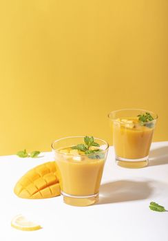 Fresh mango smoothie and ripe mango slice on yellow background. summer drink.