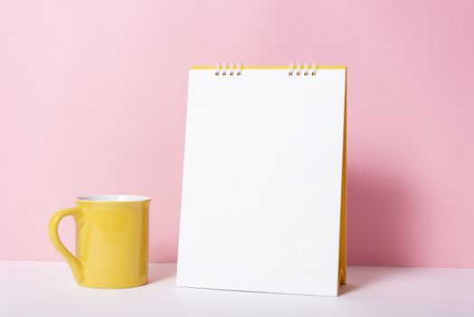 Blank paper spiral calendar with cup for mockup template advertising and branding on pink background.