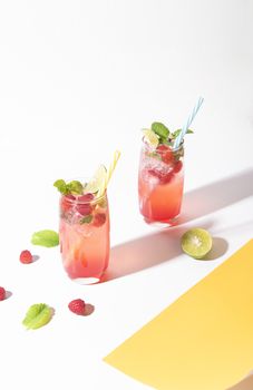 iced red raspberry punch cocktail with lime in glass on color background. summer drink.