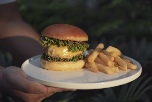 Waiters carrying dish beef burger and french fries with sunlight at restaurant.