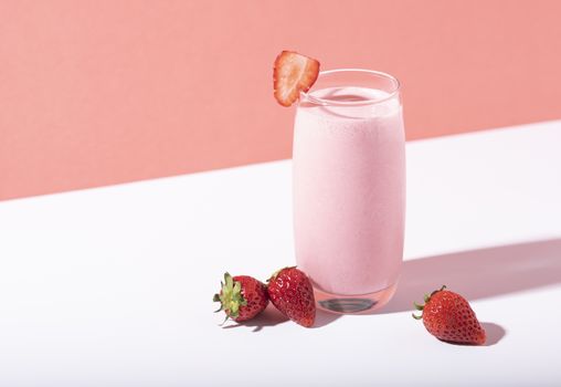 Strawberry smoothie in glass with straw and scattered berries on pink background. 