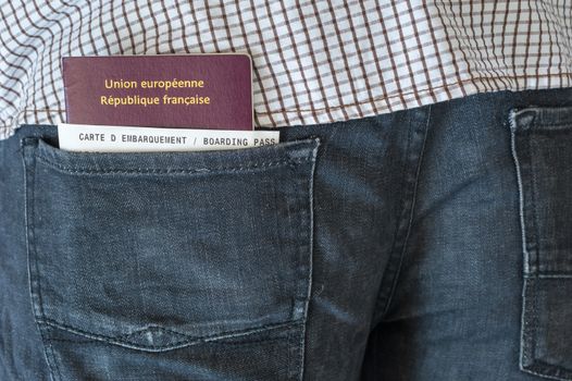 Man with a french passport and boarding pass in his blue jeans rear pocket