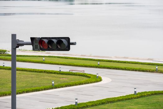 Red traffic light at a crossroads by a lake with grass in the foreground