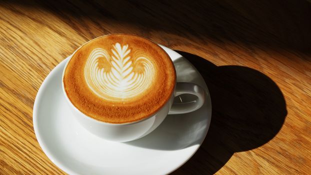 latte or Cappuccino art coffee cup top view on wood table with sunlight in cafe.