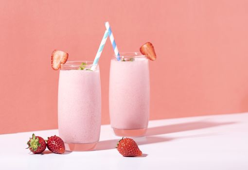 Strawberry smoothie in glass with straw and scattered berries on pink background.