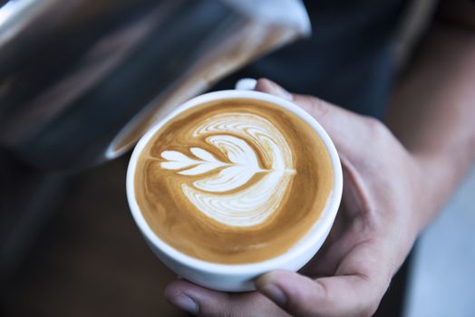 Barista making latte or Cappuccino art with frothy foam, coffee cup in cafe.